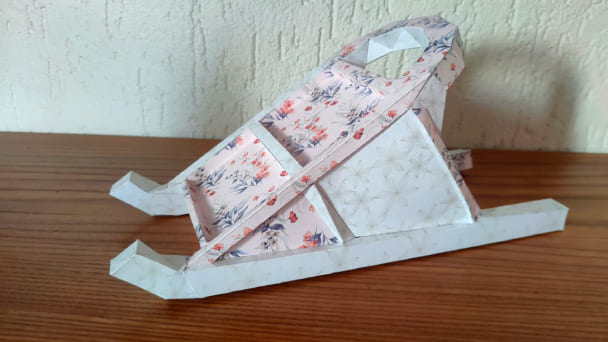 sculpture papercraft du traineau, posé sur une surface en bois. Le papercraft est assemblé avec un papier fleuri